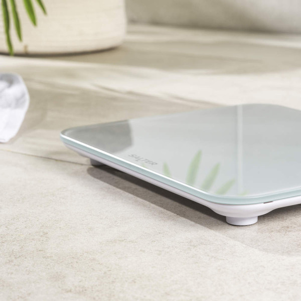 Glass digital bathroom scale with rounded corners on a tiled floor