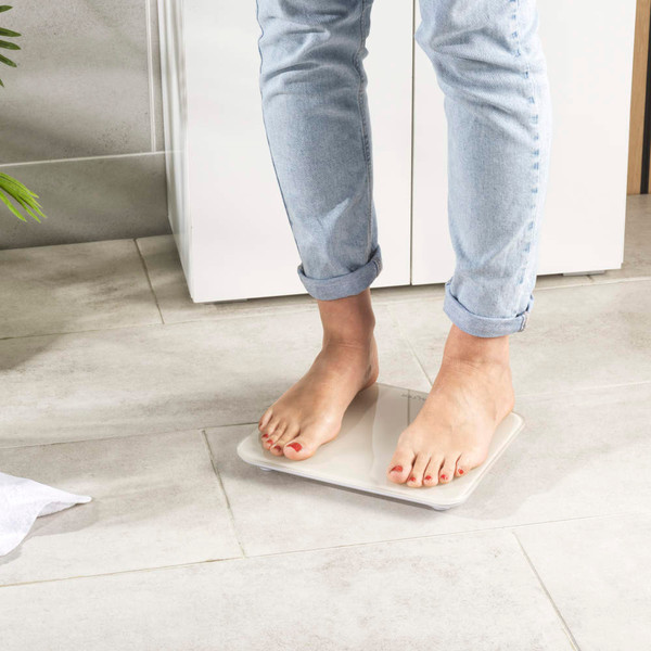 Person standing on cream bathroom scale, light tiled floor, cropped view