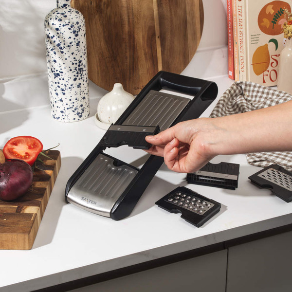 Black and silver handheld mandoline slicer with protective holder, shown slicing cucumber.