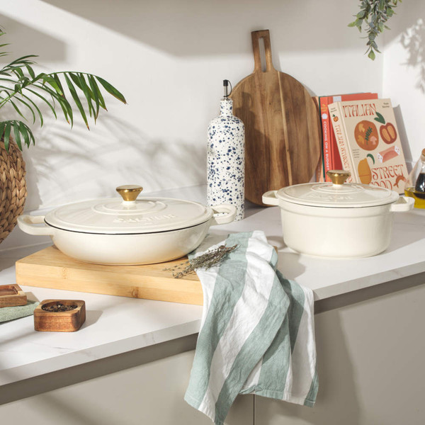 Cream cast iron casserole dish with gold handle and lid, shown from the front.