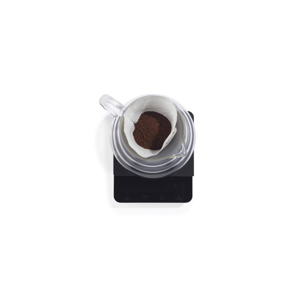 Glass coffee dripper with paper filter and ground coffee, top-down view, on digital scale