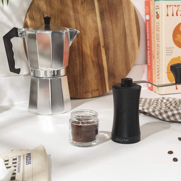 Black manual coffee grinder with side handle, clear base, shown on white background