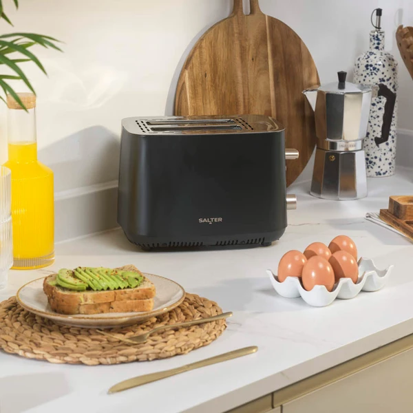 Black two-slice toaster on kitchen counter with eggs and avocado toast