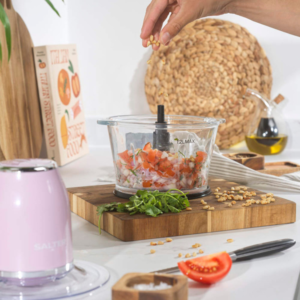 Pink electric food chopper with glass bowl, shown in use on kitchen counter