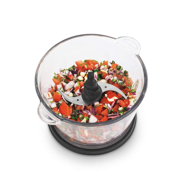 Glass food chopper bowl with diced vegetables and herbs, top view
