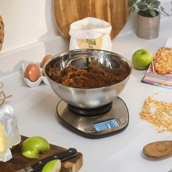 Salter kitchen scale in silver next to mixing bowl with flour, egg and whisk.