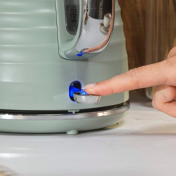 Sage green electric kettle being switched on, showing blue power light.