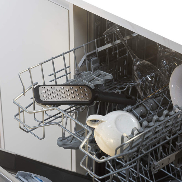 Black metal grater on top rack of dishwasher with mugs and wine glasses