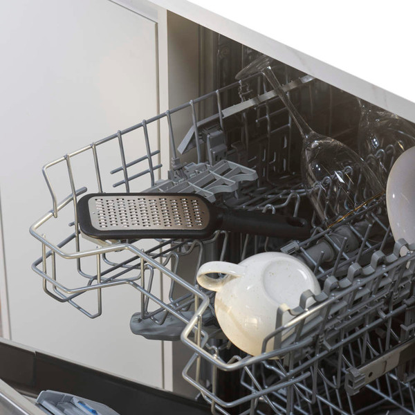 Black metal grater on top rack of dishwasher with mugs and wine glasses