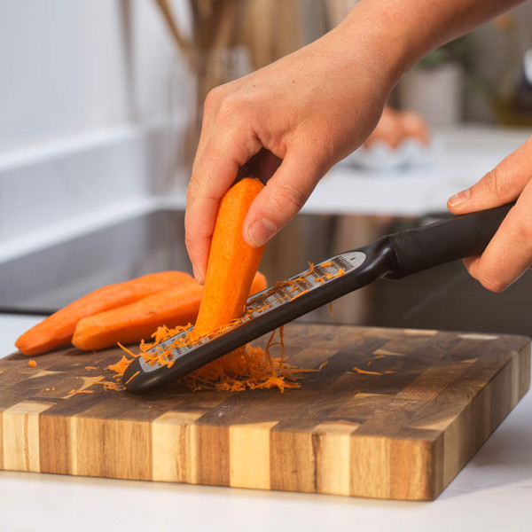 Hand grating a carrot on a cutting board in a kitchen