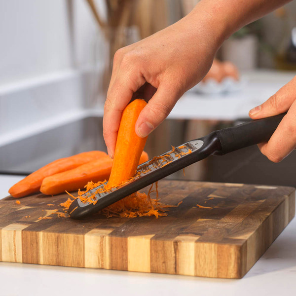 Hand grating a carrot on a cutting board in a kitchen