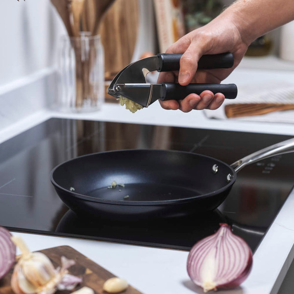 Cookware in use: non-stick frying pan on hob, minced garlic pressed in by hand