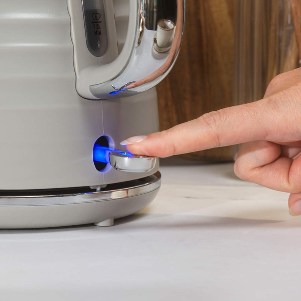 Hand pressing power switch on taupe electric kettle with illuminated blue light