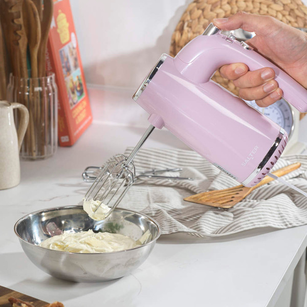 Pink hand mixer blending cream in metal bowl on a kitchen counter
