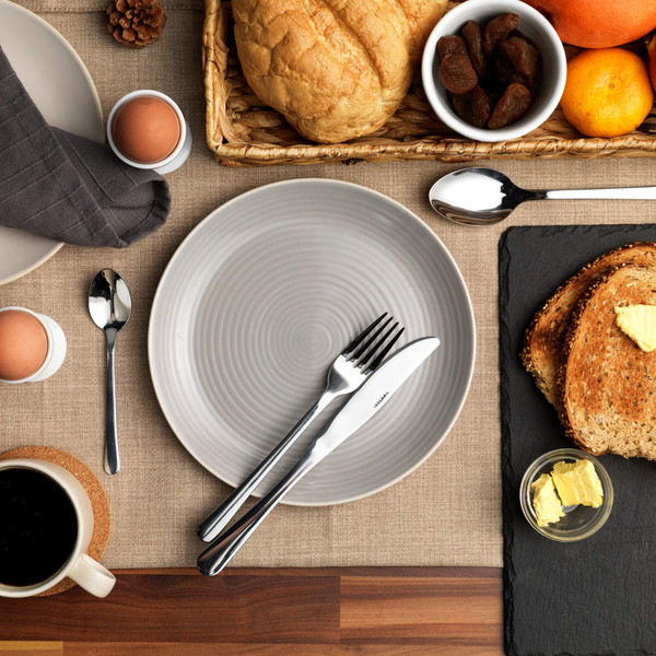 Breakfast table setting with grey plate, cutlery, eggs, toast, butter, bread, fruit, and coffee