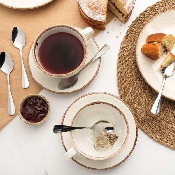 Table setting with cake, tea, ceramic crockery and stainless steel teaspoons.