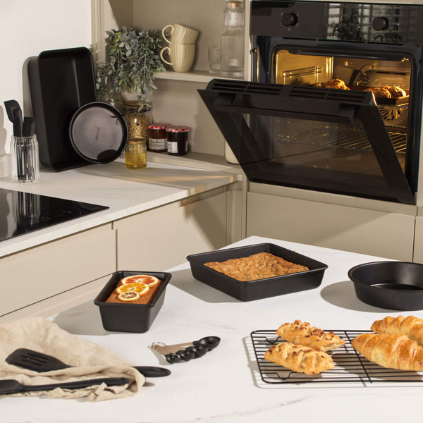 Set of black non-stick baking tins on kitchen counter, including loaf tin, with fresh bakes