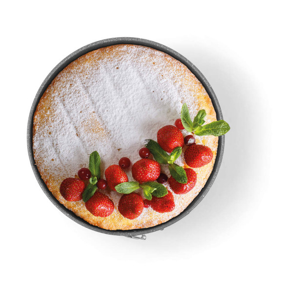 Round sponge cake topped with icing sugar, fresh strawberries, redcurrants, and mint leaves.