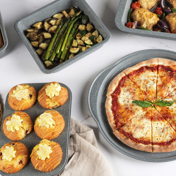 Set of grey non-stick bakeware with baked pizza, muffins, and roasted vegetables