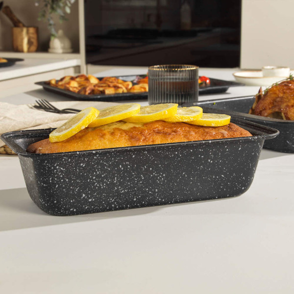 Black speckled loaf tin with baked lemon cake, shown on a kitchen counter.