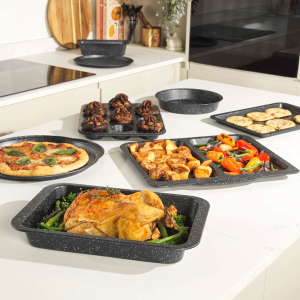 Set of grey speckled non-stick oven trays and tins shown with cooked food in modern kitchen