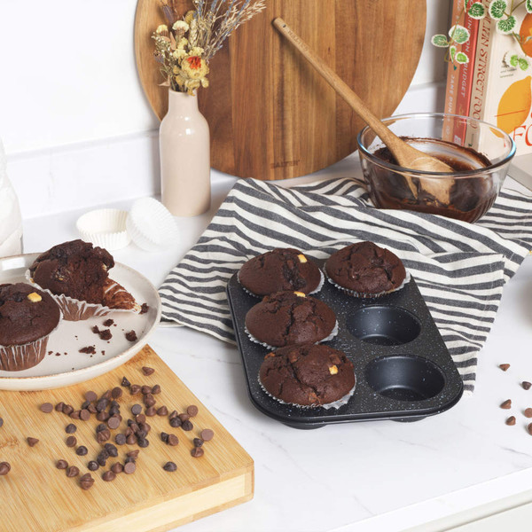 Non-stick muffin tray with four baked chocolate muffins on a kitchen counter