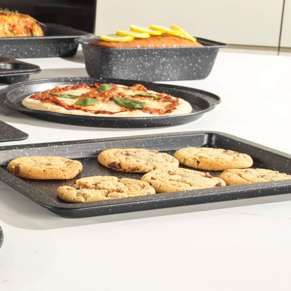 Non-stick speckled baking tray with six chocolate chip cookies, shown in kitchen setting
