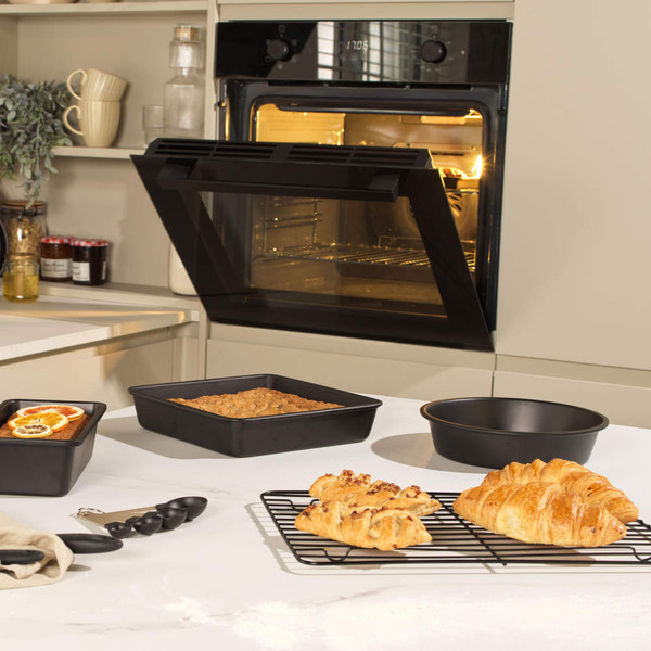 Non-stick black bakeware on kitchen counter with oven, including tin and cooling rack.
