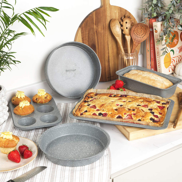 Set of grey non-stick bakeware trays with cakes and pastries, shown in a kitchen.