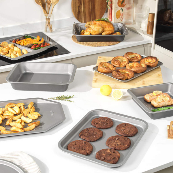 Set of non-stick grey baking trays with various baked British foods in modern kitchen.