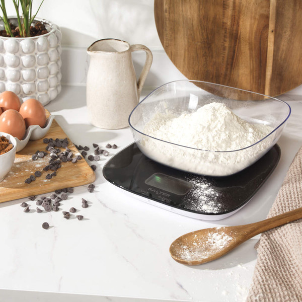 Black digital kitchen scale with assorted nuts on top, next to a bowl of mixed nuts
