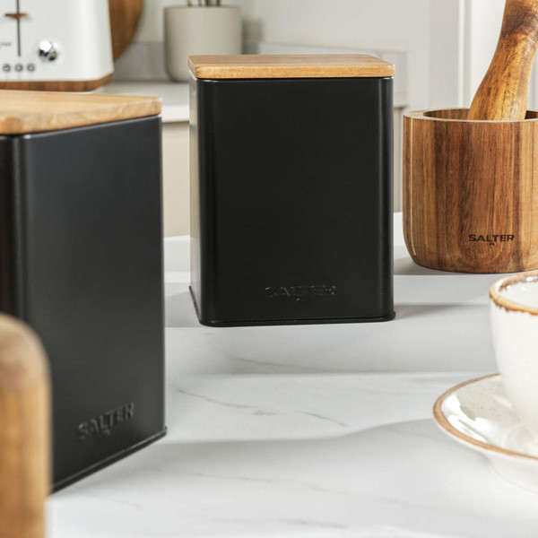 Black metal storage canister with wood lid, shown on kitchen counter