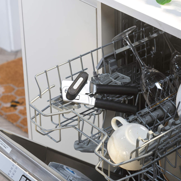 Black can opener with soft grip handles in dishwasher upper rack, next to cups and glasses