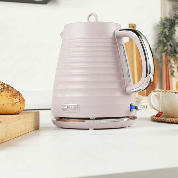 Pink ribbed electric kettle on kitchen counter, side view with chrome handle