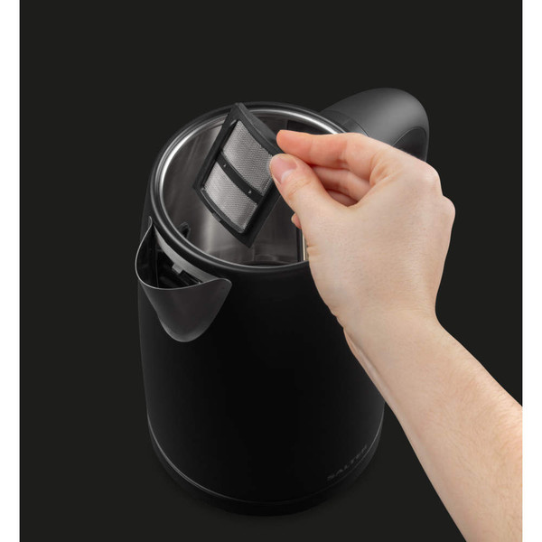 Hand removing limescale filter from black electric kettle, showing cleaning feature.