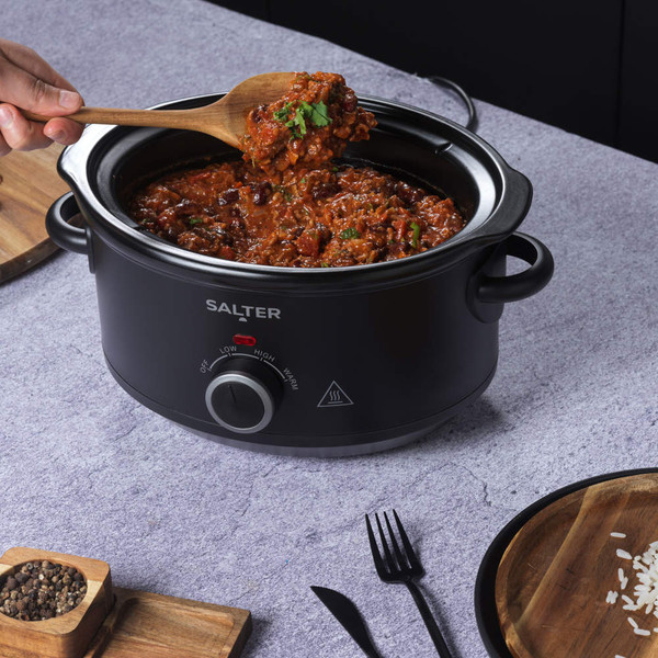 Black Salter slow cooker with chilli con carne being served, on worktop.