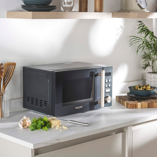 Grey microwave oven on a kitchen countertop with food and utensils nearby