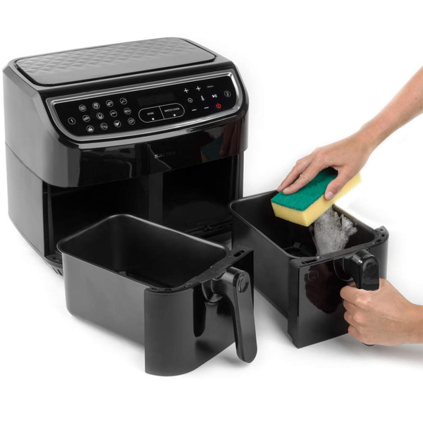 Black dual basket air fryer, one basket being washed with a sponge.