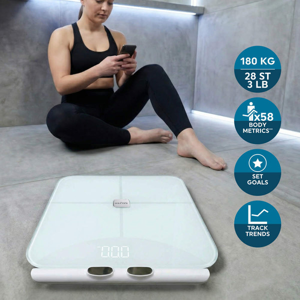 White digital bathroom scale with body metrics features, shown in use by woman after workout.