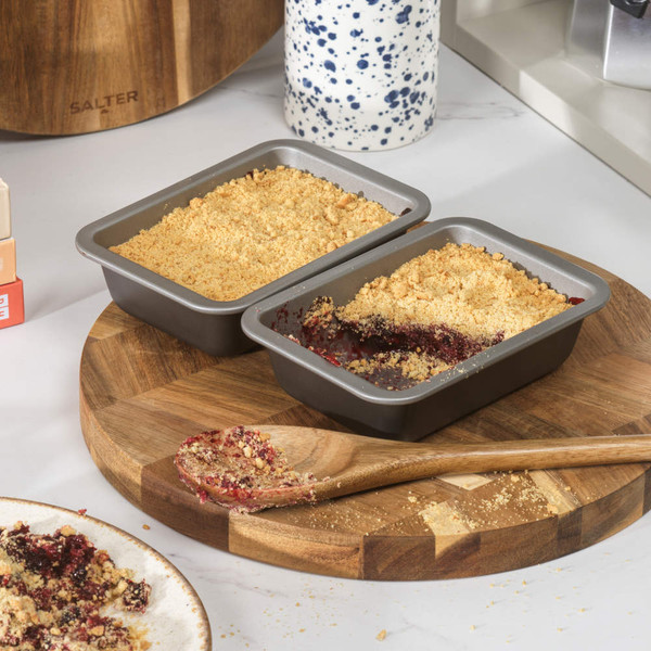 Twin grey non-stick loaf tins filled with berry crumble, one partially served