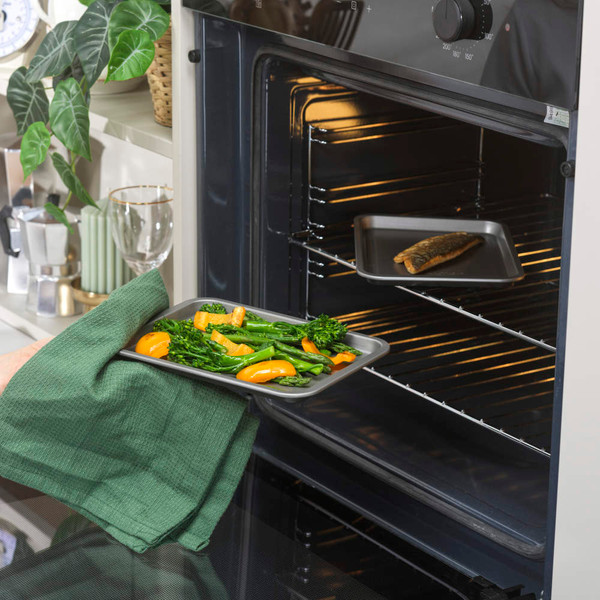Baking tray of roasted vegetables and fish being placed in oven