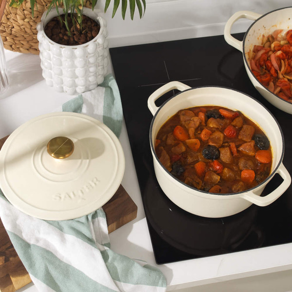 Cream cast iron casserole dish on hob, filled with beef stew and vegetables