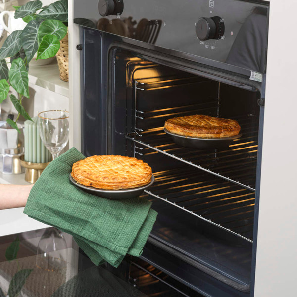 Golden pie in black baking dish, being placed in oven, kitchen background visible