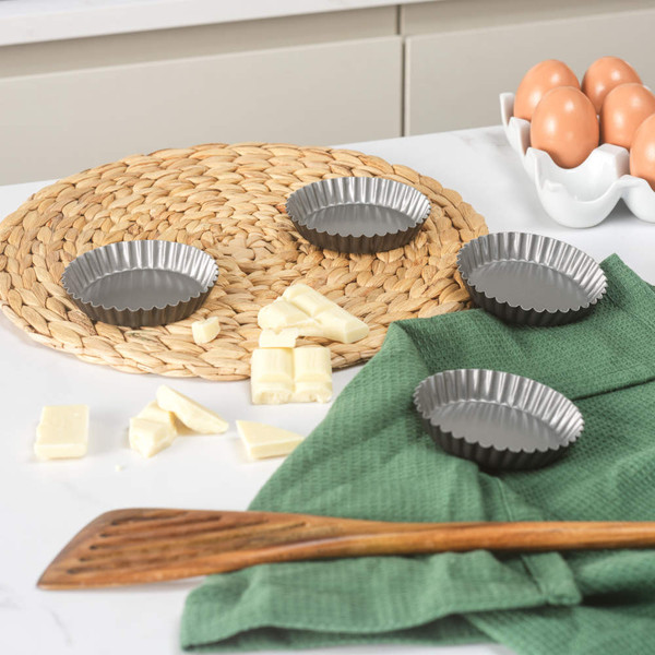 Set of four round fluted tartlet tins, grey, shown with baking ingredients.