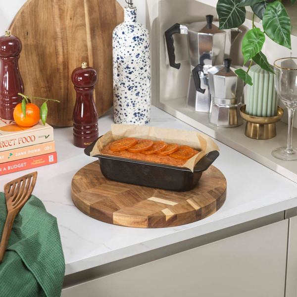 Loaf tin with baked orange-topped cake on wooden board, shown in a kitchen setting