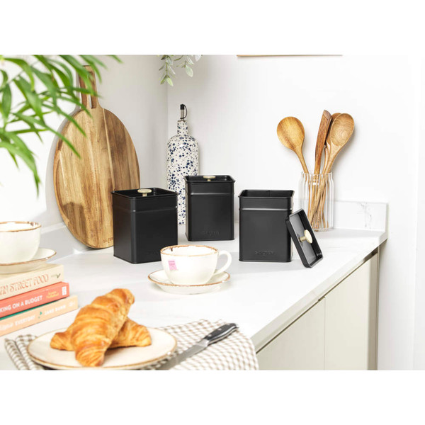 Set of three black kitchen storage canisters with lids on a white worktop