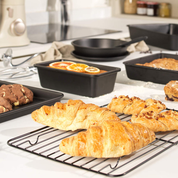 Non-stick bakeware with chocolate cookies, croissants, and loaf cake in a modern kitchen.