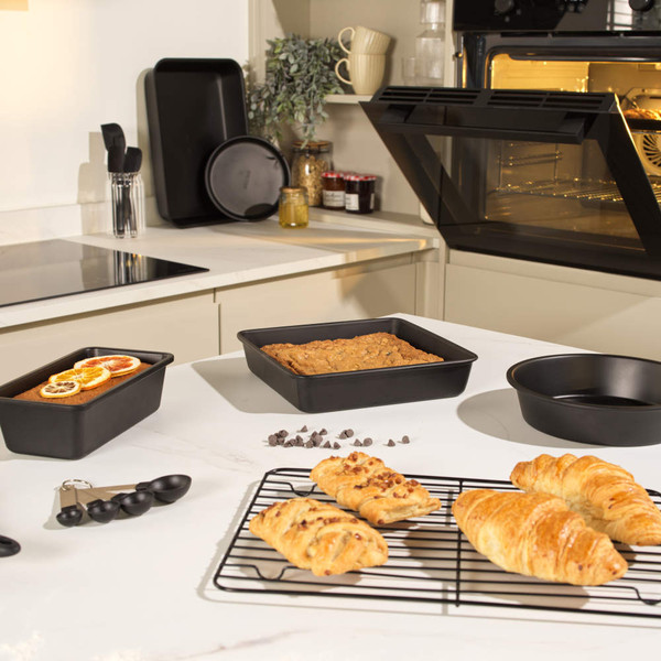 Set of black non-stick baking tins with pastries and cakes, shown in a modern kitchen.