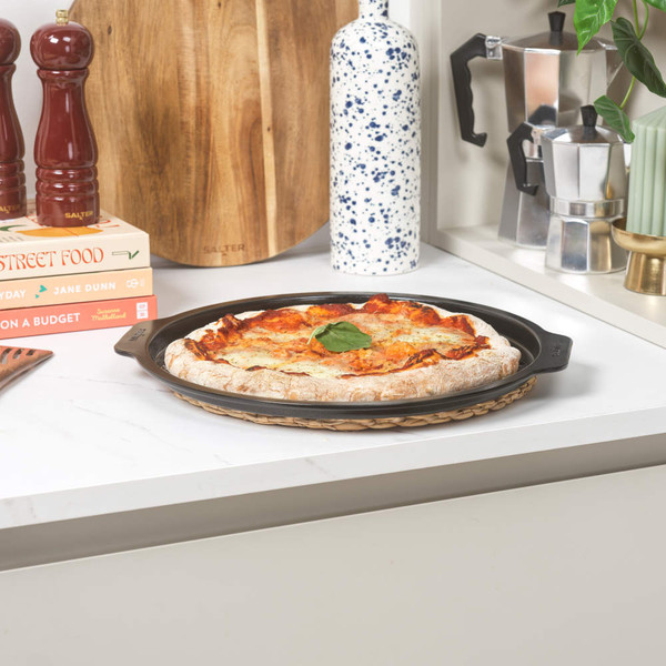 Round pizza with cheese and tomato on non-stick black pizza tray on kitchen worktop