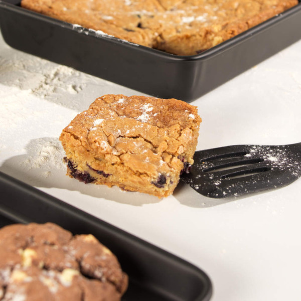Square blondie with chocolate chips in black baking tray, dusted with icing sugar